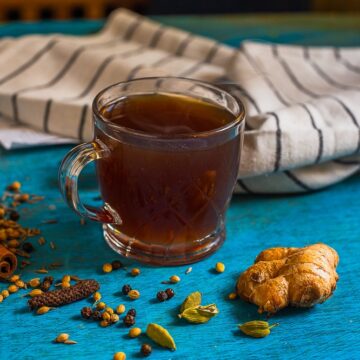 Kashayam in a glass cup with all ingredients scattered on the board